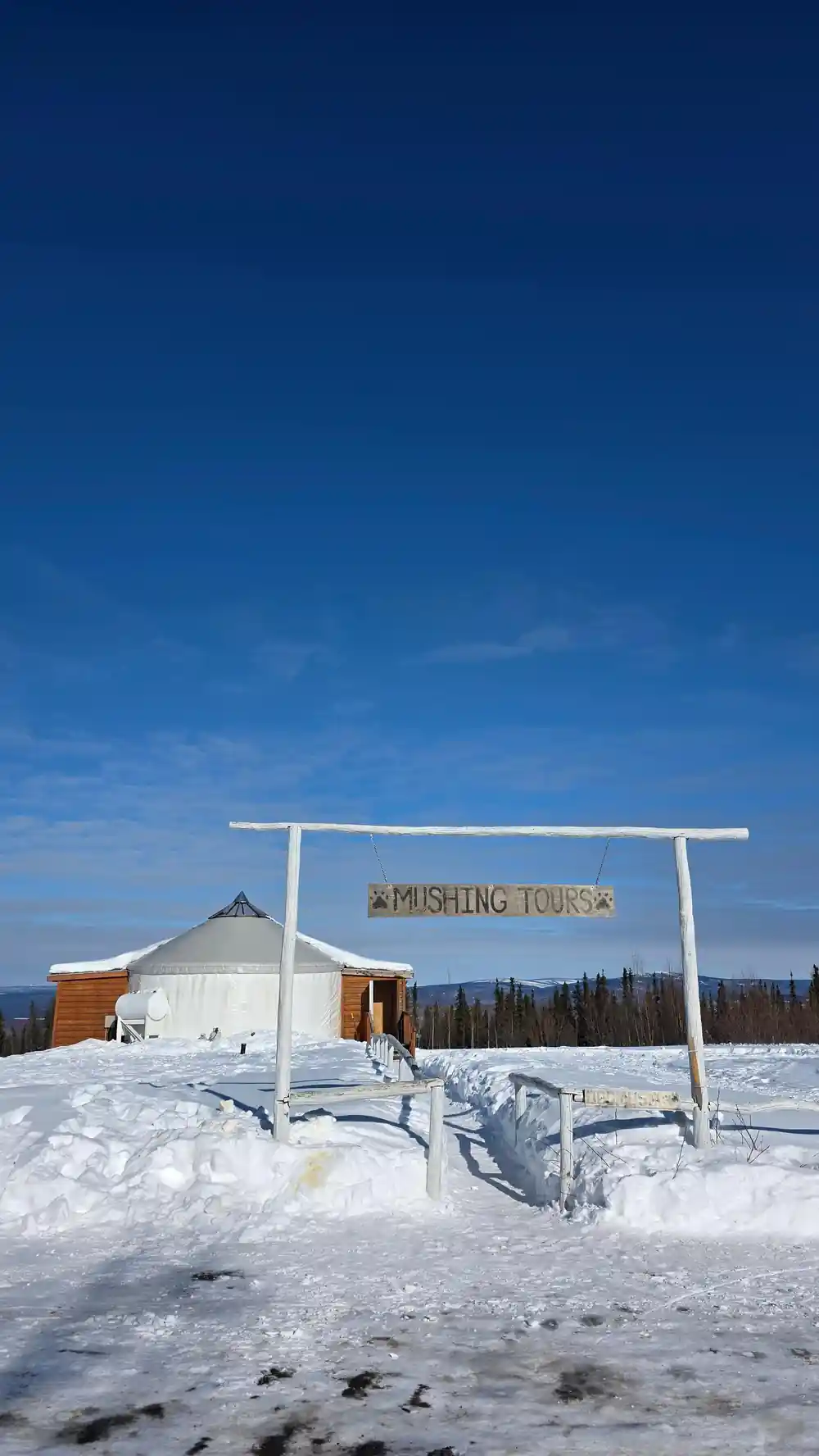 A timber gateway reading Mushing Tours with a yurt behind it