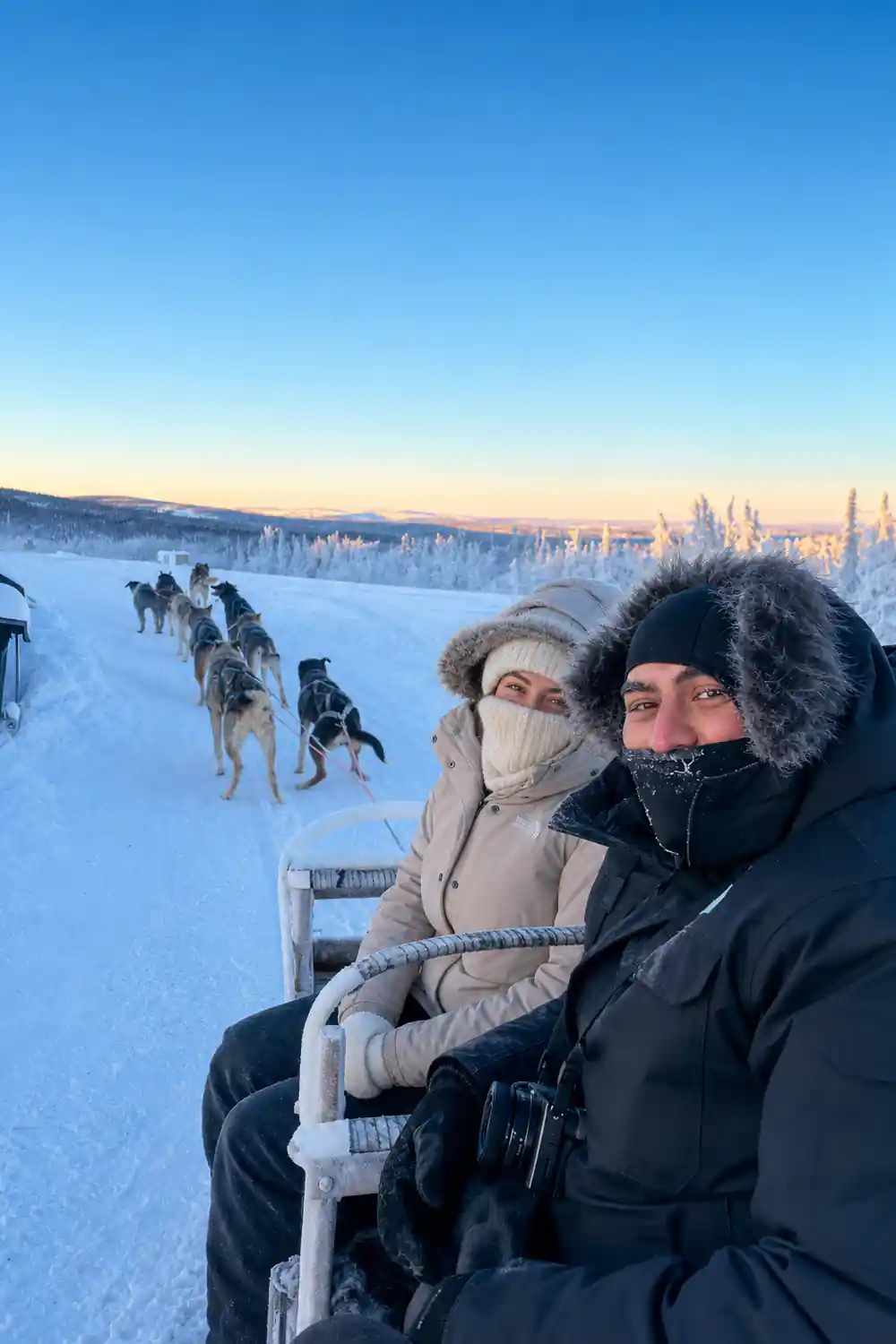 Two passengers in a sled at dawn with the team ahead