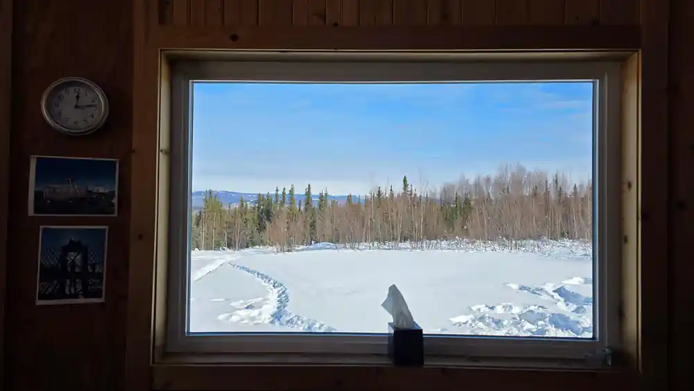 A window looking out over snow from inside a timber building